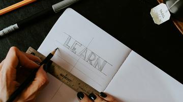A person's hands against a note book where the word LEARN is written. 